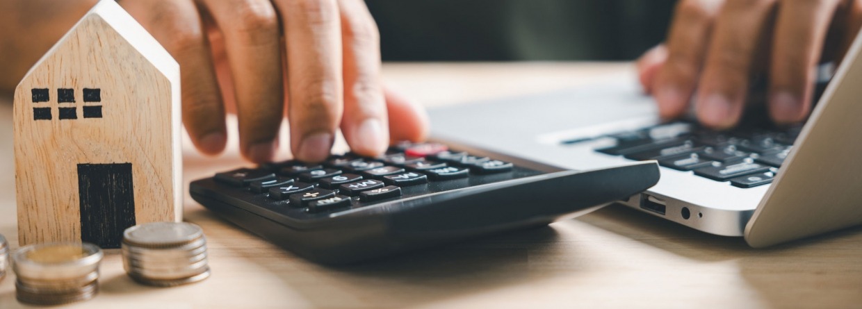 Een man is aan het rekenen op een rekenmachine met op de voorgrond een huisje en munten